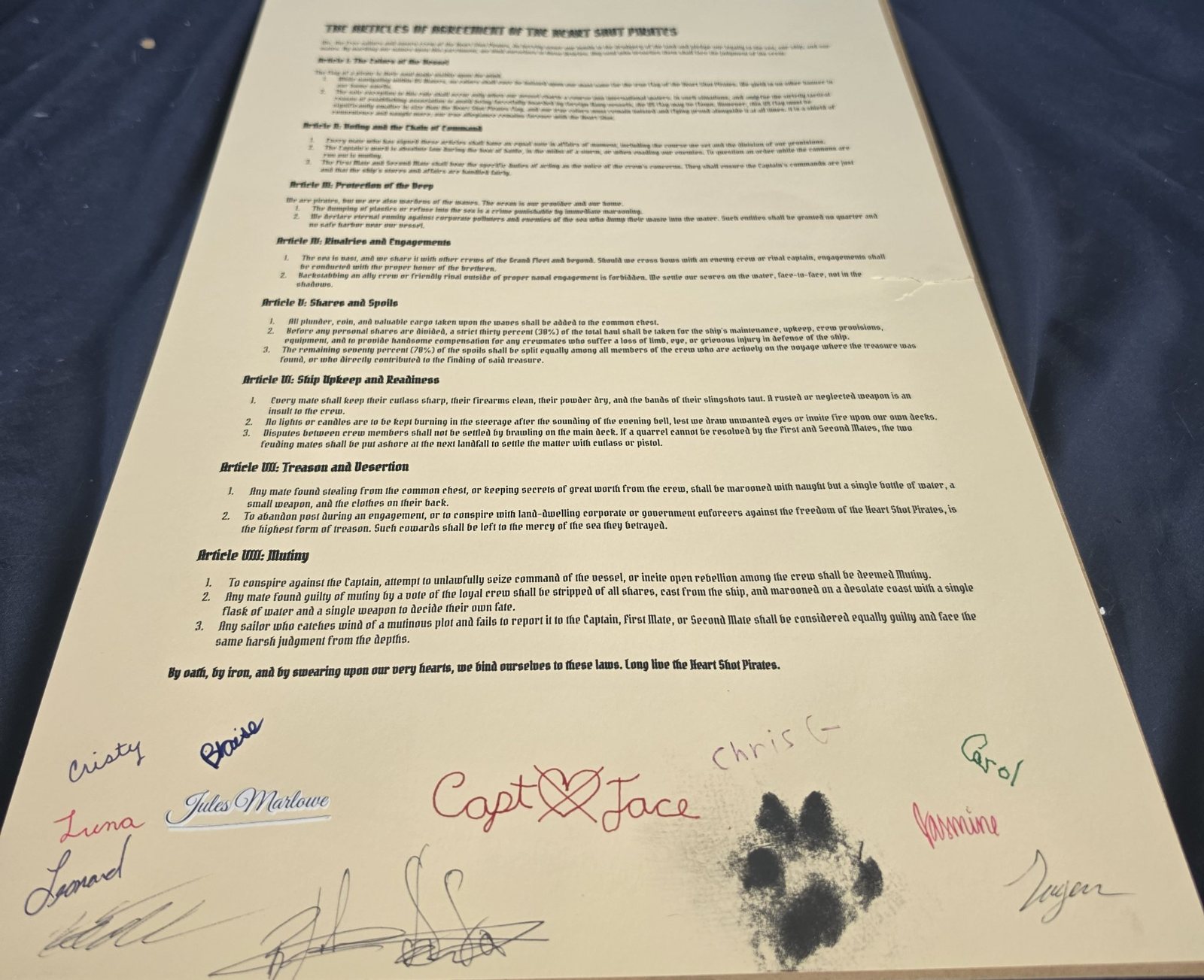 The Articles of Agreement of the Heart Shot Pirates: the printed articles on parchment, signed at the foot by the crew — Cristy, Blaise, Luna, Jules Marlowe, Captain Jace, Chris, Carol, Jasmine, Leonard, and the First Mate's paw print.